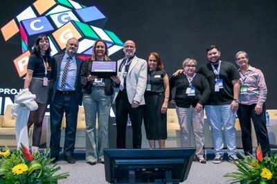 Equipe da CGPAG/DECIPEX no palco, recebendo o prêmio de 1º lugar em Experiências Inspiradoras em Gestão de Pessoas, com o telão da cerimônia ao fundo